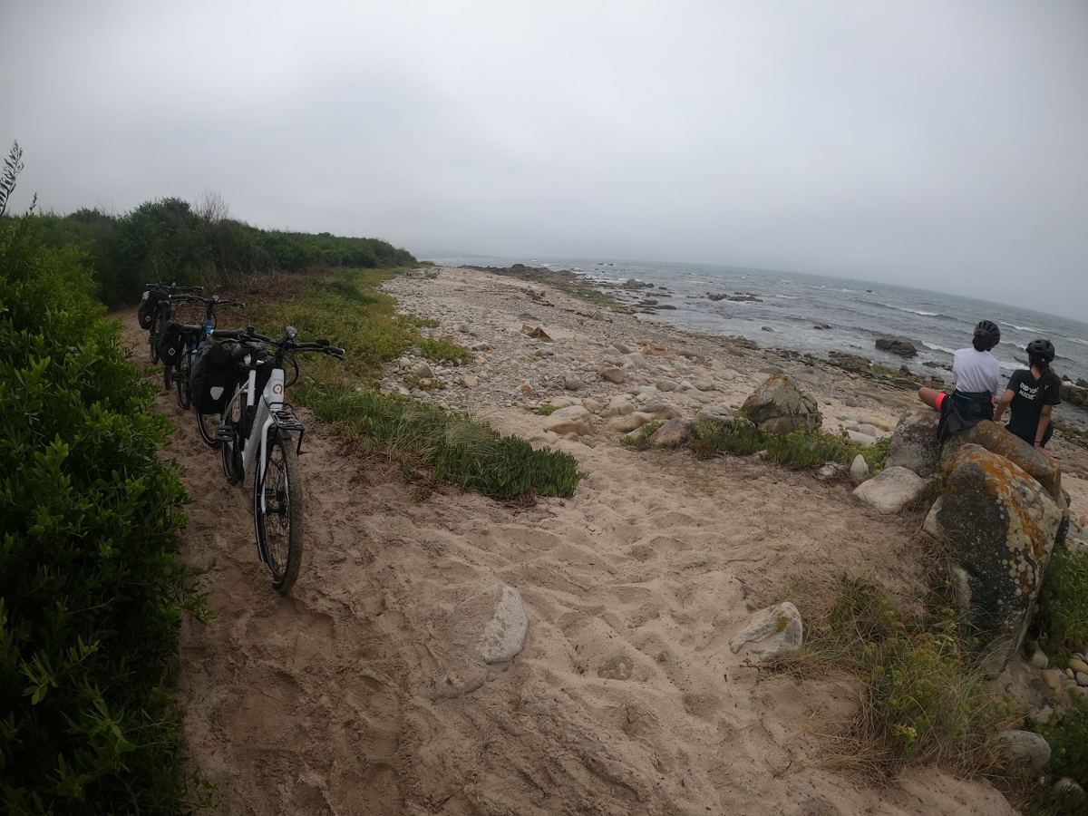 Bicicletas paradas junto a uma praia de pedras, com as filhas sentadas a olhar o mar
