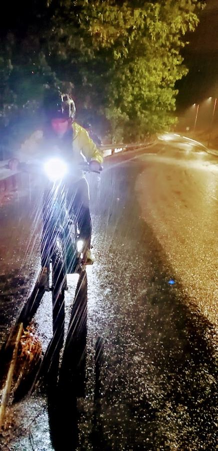 Ciclista à noite, debaixo de chuva, com a luz da bicicleta acesa