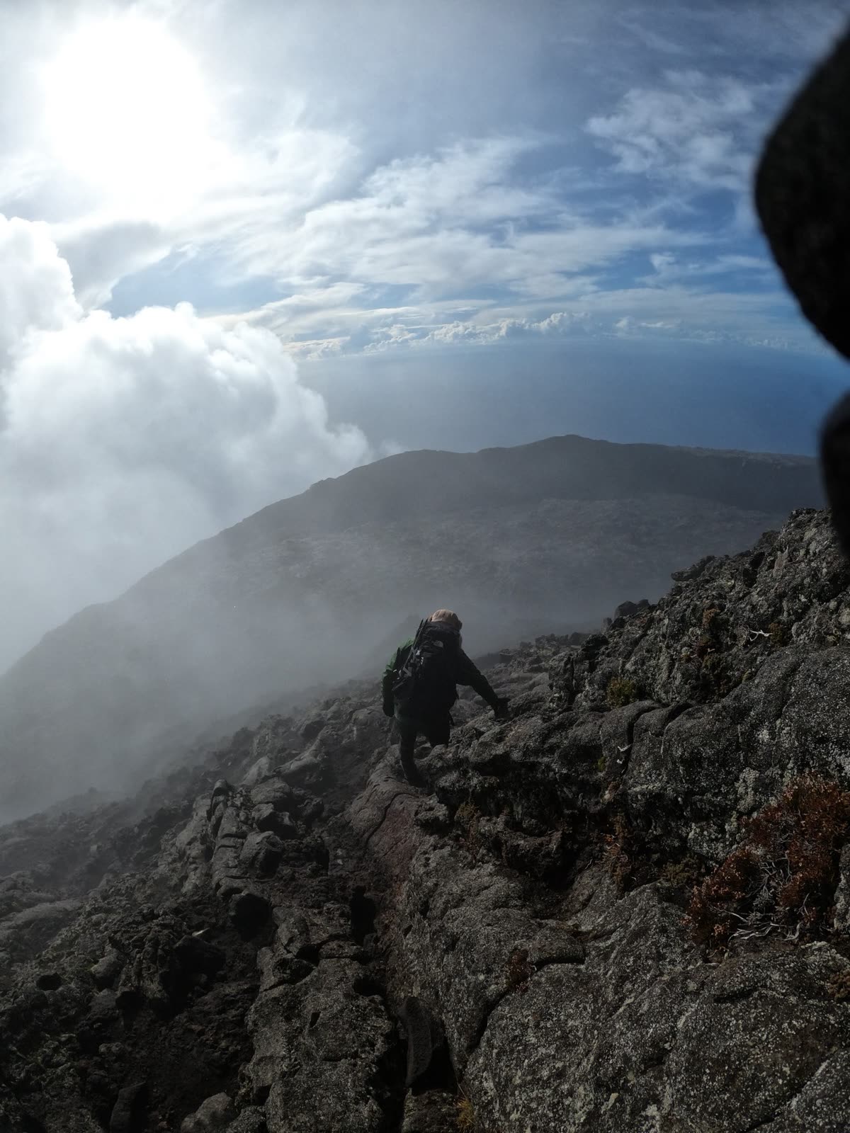 Scrambling over lava, with clouds rising up the slope and the sea below