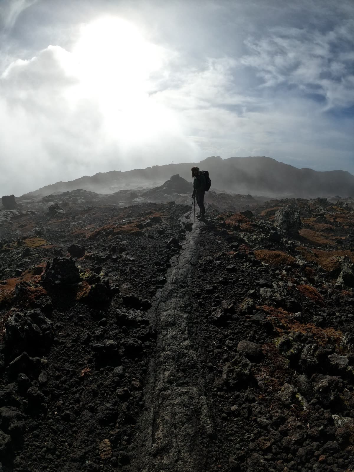 Silhouette of a hiker on a lava path, with the sun breaking through the mist
