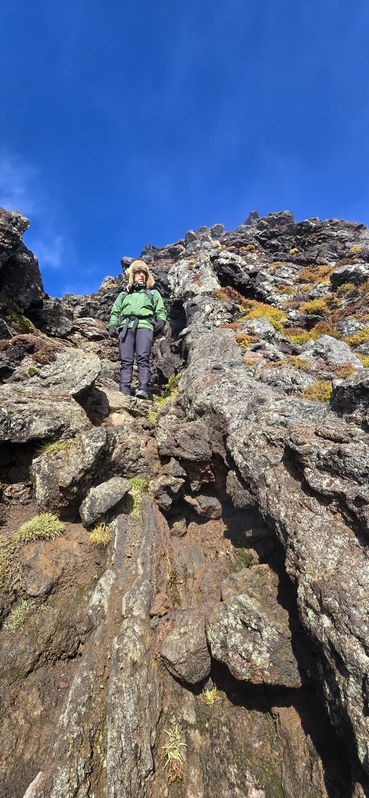 Hiker in a green jacket at the top of a rock wall, under a blue sky