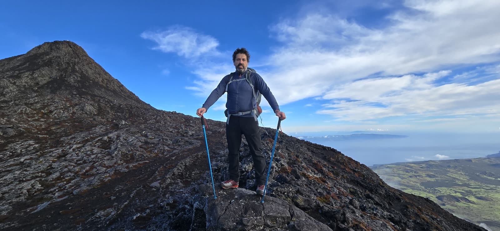 José with trekking poles on the slope, with the summit of Pico behind and Faial on the horizon