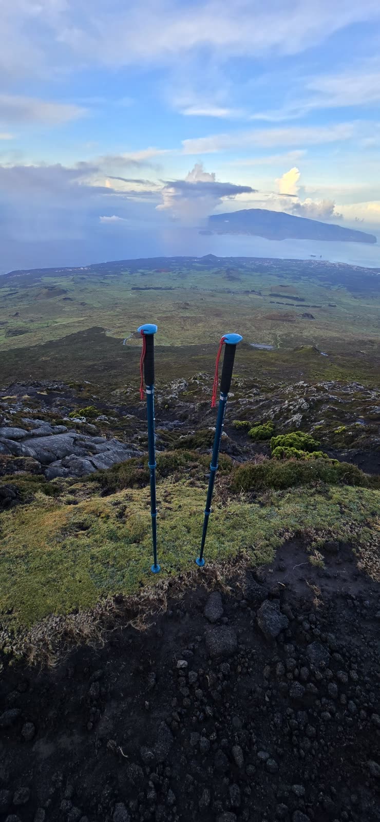 Two trekking poles planted on the slope, with Faial in the distance