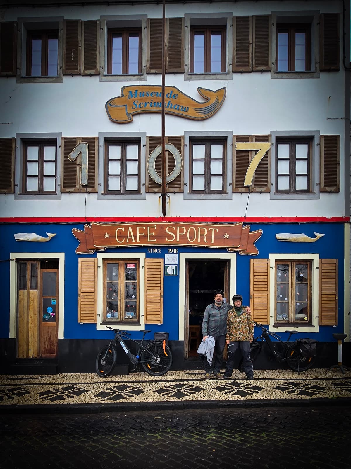 José and Cláudio at the door of Peter Café Sport, with the BEEQ bikes against the blue façade